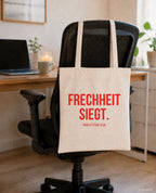 Frechheit siegt. – Stoffbeutel mit Spruch beige, am Bürostuhl im Büro
