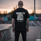 ENEMIES TO LOVERS. MOSTLY ENEMIES. – schwarzes Oversize T-Shirt mit weißem Backprint, Herren im Skatepark