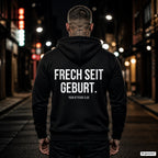 FRECH SEIT GEBURT. – schwarzer Hoodie mit weißem Backprint, Herren in der Stadt bei Nacht