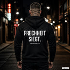 FRECHHEIT SIEGT. – schwarzer Hoodie mit weißem Backprint, Herren in der Stadt bei Nacht