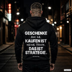 Geschenke am 24. kaufen ist keine Panik. Das ist Strategie – schwarzer Hoodie mit weißem Backprint, Herren in der Stadt bei Nacht