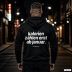 Kalorien zählen erst ab Januar – schwarzer Hoodie mit weißem Backprint, Herren in der Stadt bei Nacht