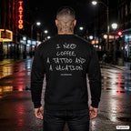 I need coffee, a tattoo and a vacation – schwarzer Pullover mit weißem Backprint, Herren in der Stadt bei Nacht