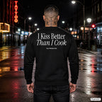 I kiss better than I cook – schwarzer Pullover mit weißem Backprint, Herren in der Stadt bei Nacht