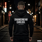 UNANGENEHM EHRLICH. – schwarzer Hoodie mit weißem Backprint, Herren in der Stadt bei Nacht