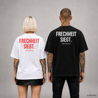 FRECHHEIT SIEGT. – Oversize T-Shirt Unisex mit Backprint, Frau in Weiß mit rotem und Mann in Schwarz mit weißem Aufdruck