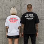 ICH BEREUE NICHTS. AUSSER MENSCHEN. – Oversize Shirt mit Spruch auf dem Rücken, Paar in Weiß und Schwarz vor Betonwand