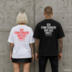 ICH FUNKTIONIERE NUR AUS TROTZ. – Oversize Shirt mit Spruch auf dem Rücken, Paar in Weiß und Schwarz vor Betonwand