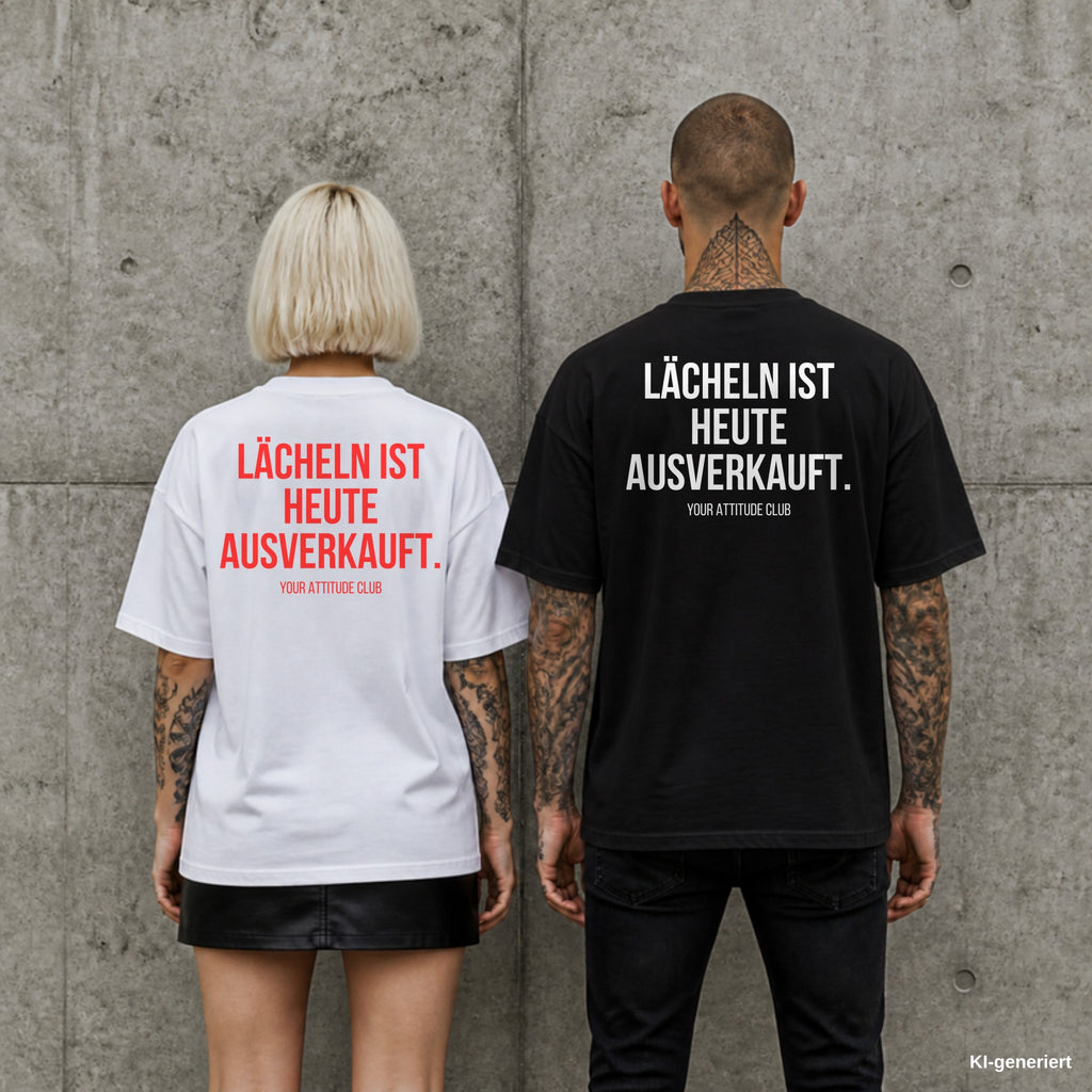 LÄCHELN IST HEUTE AUSVERKAUFT. – Oversize Shirt mit Spruch auf dem Rücken, Paar in Weiß und Schwarz vor Betonwand