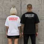 SCHWIERIG? NEIN. ANSPRUCHSVOLL. – Oversize Shirt mit Spruch auf dem Rücken, Paar in Weiß und Schwarz vor Betonwand