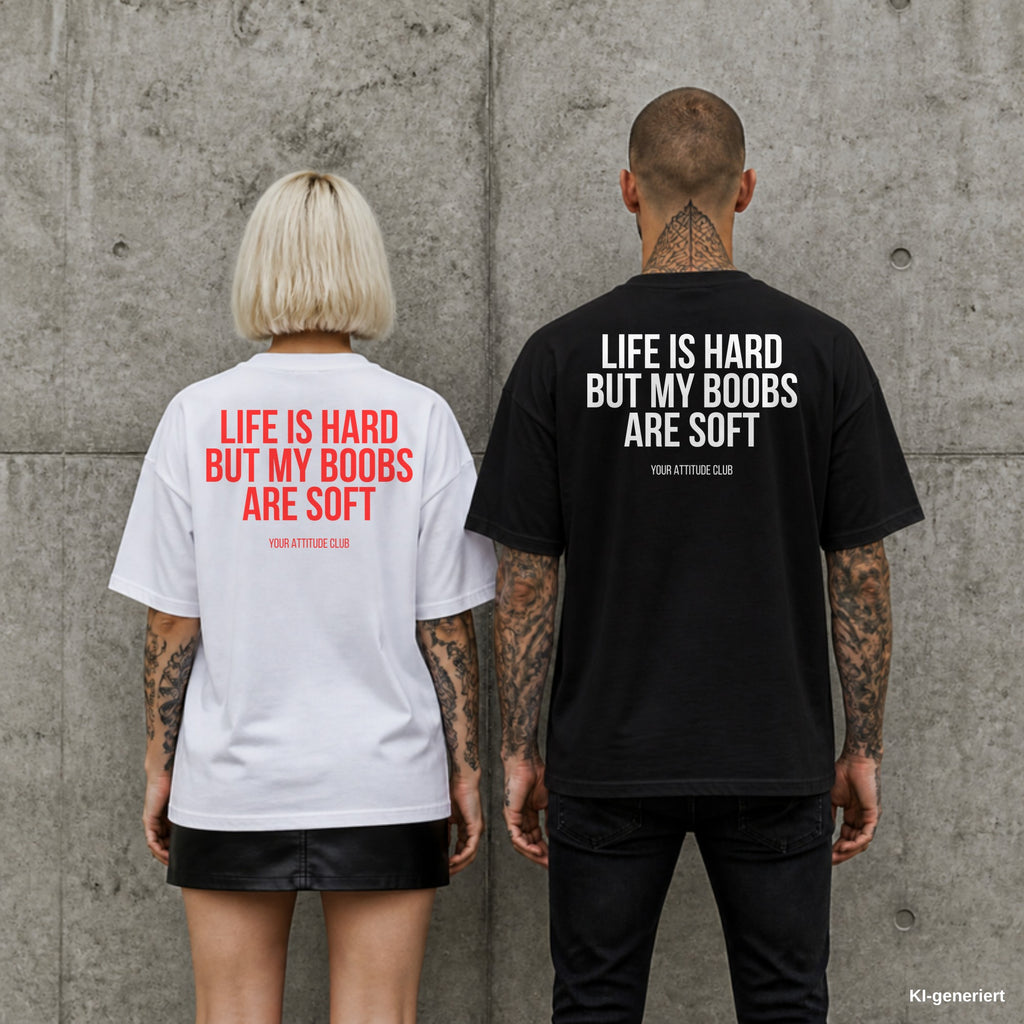 LIFE IS HARD BUT MY BOOBS ARE SOFT – Oversize Shirt mit Spruch auf dem Rücken, Paar in Weiß und Schwarz vor Betonwand