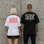 LET’S FALL IN LOVE IN THE CLUB TOILETS – Oversize Shirt mit Spruch auf dem Rücken, Paar in Weiß und Schwarz vor Betonwand