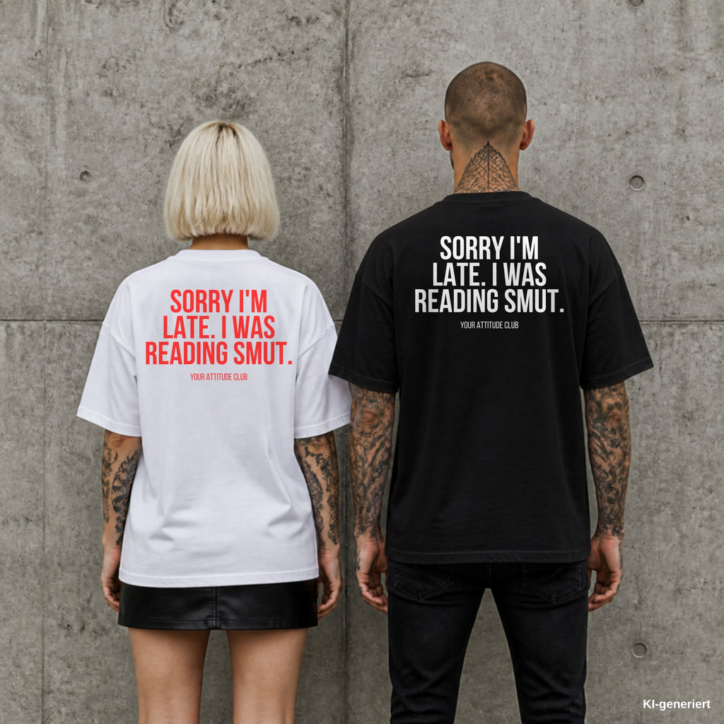 SORRY I'M LATE. I WAS READING SMUT. – Oversize Shirt mit Spruch auf dem Rücken, Paar in Weiß und Schwarz vor Betonwand