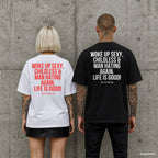WOKE UP SEXY, CHILDLESS & MAN HATING AGAIN. LIFE IS GOOD! – Oversize Shirt mit Spruch auf dem Rücken, Paar in Weiß und Schwarz vor Betonwand